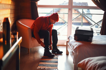 Man traveller on a winter trip wearing red clothes sitting in a hotel room, tying shoelaces