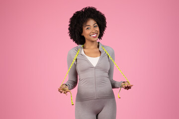 Sporty woman with measuring tape on pink background
