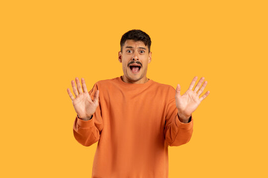 Surprised man with raised hands on orange