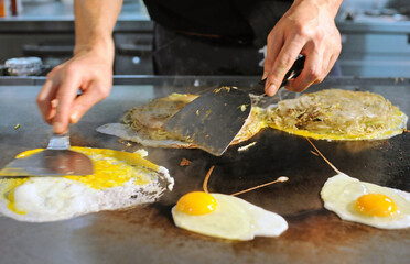 A cook is cooking eggs for okonomiyaki on a griddle