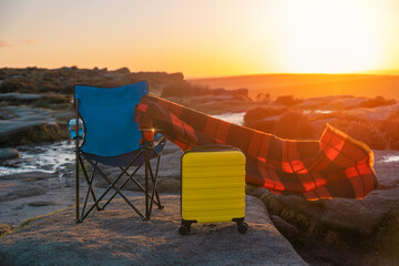 Blue beach chair, yellow  Suitcase, orange scarf on top of mountain at sunrise. Travel insurance...