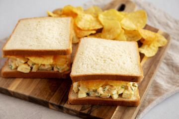 Fototapeta na wymiar Homemade Egg Salad Sandwich with Potato Chips on a wooden board, side view.