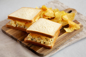 Homemade Egg Salad Sandwich with Potato Chips on a wooden board, side view. - 785667984