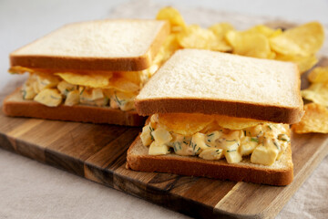 Homemade Egg Salad Sandwich with Potato Chips on a wooden board, side view. Close-up.