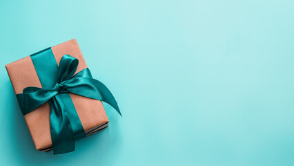 Gift box in craft wrapping paper and green satin ribbon on turquoise blue background, copy space...