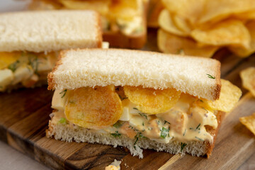 Homemade Egg Salad Sandwich with Potato Chips on a wooden board, side view. Close-up.
