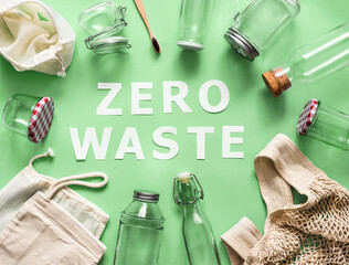 Zero waste concept. Textile eco bags, glass jars and bamboo toothbrush on green background with Zero Waste white paper text in center. Eco friendly and reuse concept. Top view or flat lay