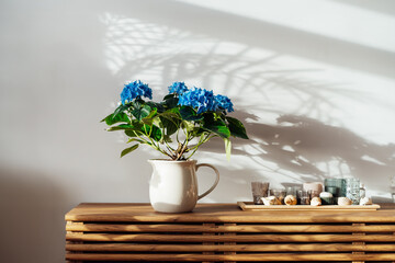 Modern minimalist Scandinavian style interior. Candles on tray and House plant blue hydrangea in a...
