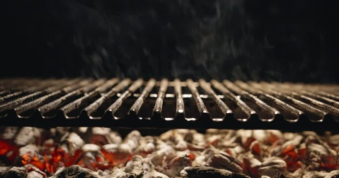 Fragrant smoke from hot coal rises above grill grate. Hot coal on dark background burns bright red. It's time for summer parties with friends and delicious, smoky, aromatic dishes, template for title 