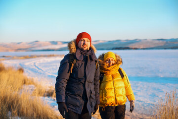 Romantic couple of tourists dressed in warm winter sportswear with tourist backpacks walking in the...