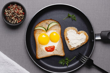 Heart shaped fried eggs with toast in frying pan on grey table, top view