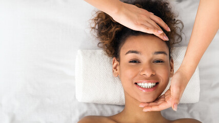 African-american woman enjoying face massage at beauty salon