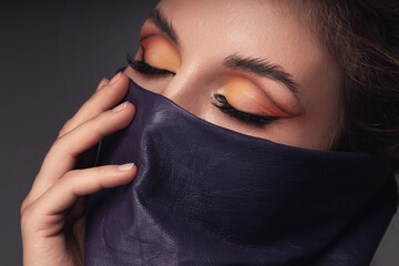 Portrait of a woman with striking eye makeup and leather wild rag covering her face