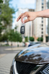 Hand with car keys, man holding key in front of new car