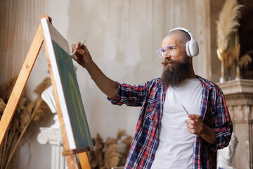 Moving paint brush artist works on abstract oil painting in creative modern studio. Guy with headphones listening to music. Abstract Modern Art.