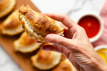 A female hand holding a typical Argentinian beef empanada. 