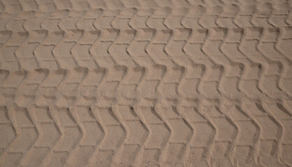 A sandy surface with a pattern of tire tracks. Scene is somewhat rugged and rough