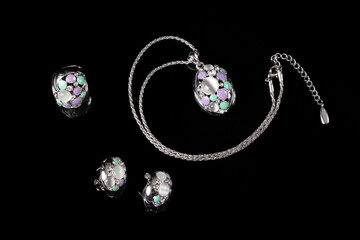 A set of silver jewelry with stones consisting of earrings, a ring and a pendant on a chain isolated on a black background.