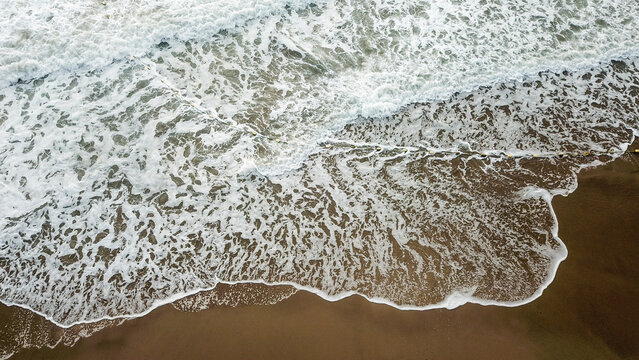 Aerial view of sandy beach and ocean with waves
