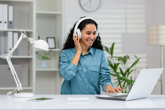 Happy woman enjoys listening to music while working on her laptop in a well-lit home office environment, showcasing productivity and comfort.