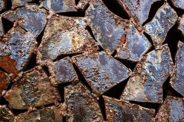 Shards of metal welded together with a lot of rust and holes. The metal is cut into small pieces and has a rough texture. Scene is one of decay and abandonment