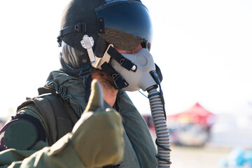 A man in a military, in pilot suit uniform is giving a thumbs up sign. He is wearing a pilot mask