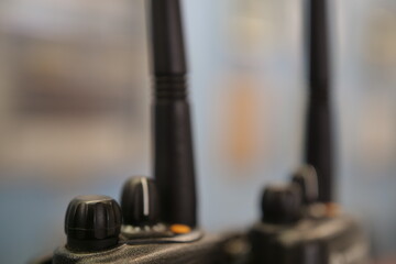 Close-up of a number of black walkie-talkie radios in front of a blurred industrial background.