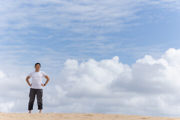 A woman stands on a beach with a cloudy sky in the background