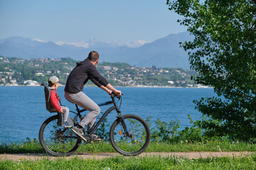 a man with a child on a mountain bike in motion with a lake in the background, mountain peaks in the snow.