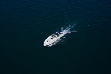 A large white boat with a blue awning moves on blue water, top view. White high-speed motor boat with people moving on the water, air view.