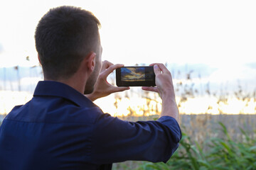  A man takes a photo of nature at sunset with his mobile phone