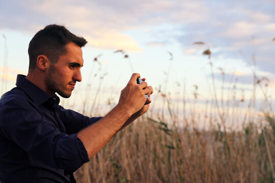 A man takes a photo of nature at sunset with his mobile phone