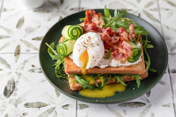 Toasts sandwich with poached egg, cucumber, arugula, bacon and cream cheese on printed tile background. Healthy breakfast, copy space