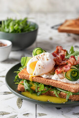 Toasts sandwich with poached egg, cucumber, arugula, bacon and cream cheese on printed tile kitchen background for healthy breakfast