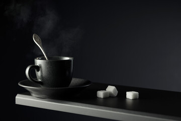 Black cup of coffee and sugar on a black background.