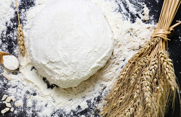 Raw dough flour and ears of wheat on black background top view Home baking concept
