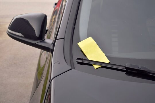 A yellow fine ticket under the car wiper.  The vehicle is parked in the wrong place or the parking time has expired.
