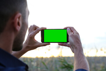 A man takes photos of nature at sunset with his mobile phone. Traveler man taking landscape photos...