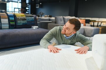 Young male customer examining orthopedic mattress on sale at furniture store, copy space