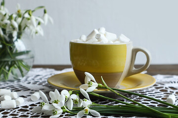 Spring tea party: airy marshmallows in a yellow cup against the background of a bouquet of snowdrops