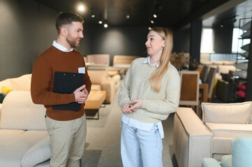 Young salesman helping customer to choose new modern sofa in store