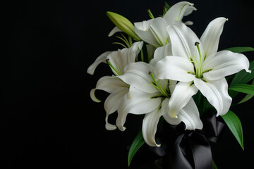 Black funeral ribbon and white lily flowers on dark background