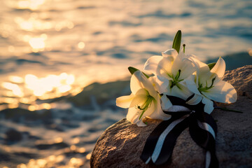 Black funeral ribbon and white lily flowers on a rock by the calm sea - obrazy, fototapety, plakaty