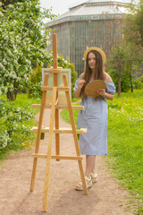 Beautiful female artist painting on canvas and wooden easel in spring botanical garden. Art process...