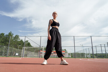 A confident, athletic young woman with tattoos stands on a red running track, exuding determination...