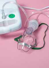 A clear plastic mask with a green strap is on a pink background. The mask is connected to a tube...
