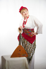 Cheerful funny adult mature woman solokha with musical balalaika. Female model in clothes of...
