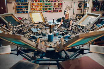 Female graphic worker operating screen carousel printing press at factory