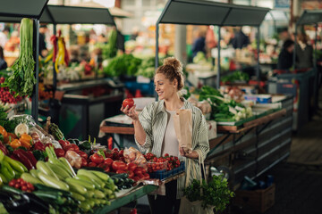 Smiling customer buying fresh tomato at organic food marketplace.