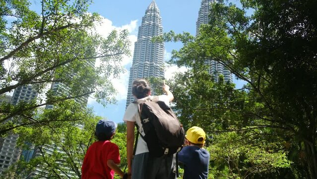 Mother with two children aged 5 and 7 in front of the Petronas Towers in Kuala Lumpur, exploring the Southeast Asian city. Single mother trip with children to Asia summer adventures family adventures 